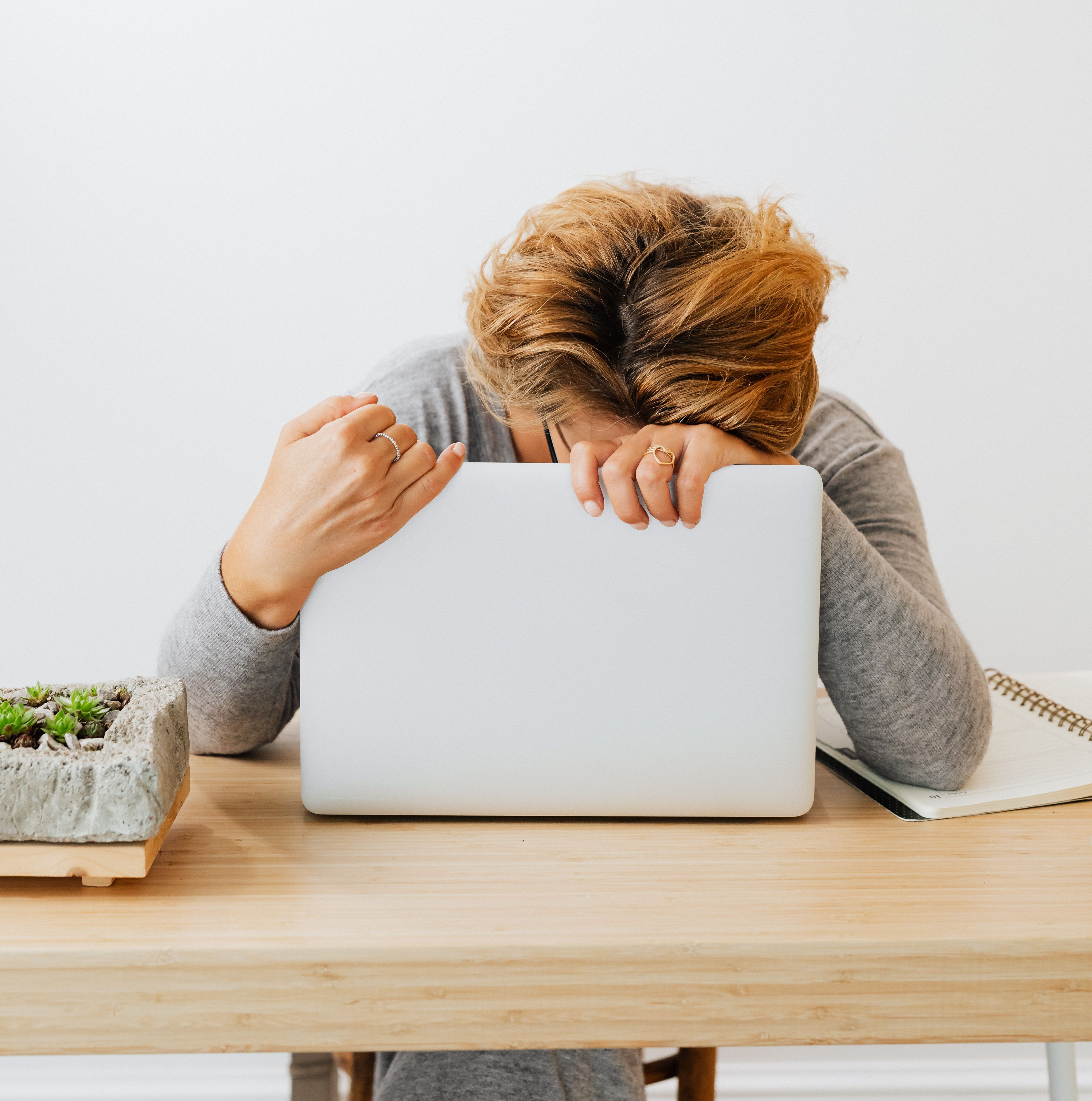 Woman resting her head on her laptop, fatigued